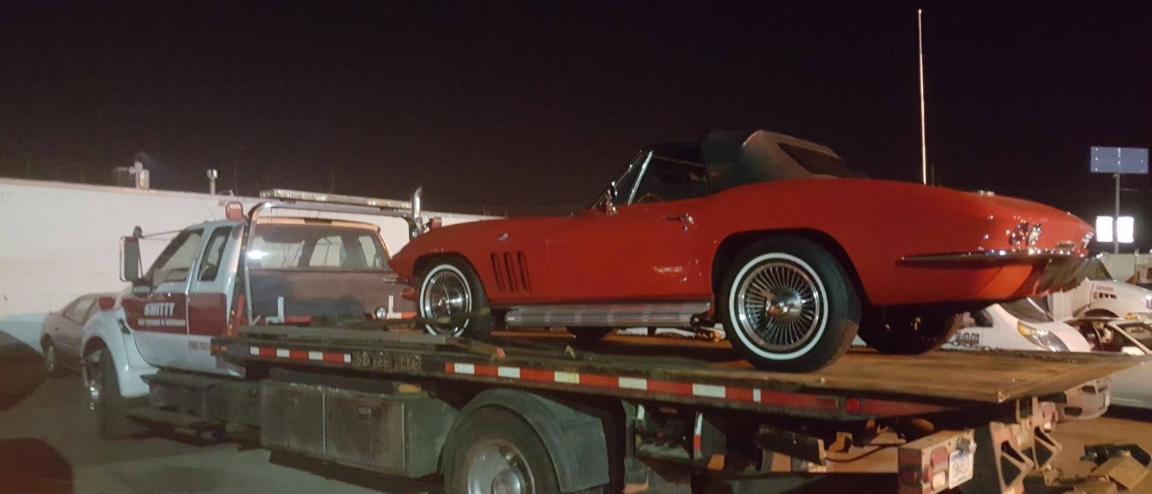 Vintage red Corvette loaded on flatbed at night